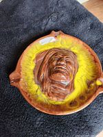 Ceramic ashtray featuring a raised face of a Native American with brown and yellow glaze.