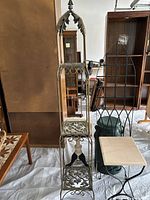 Full view of the ornate painted plant stand with claw feet and floral detailing, also showing nearby wood furniture and the trellis behind.