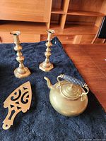 Pair of brass candlesticks, brass teapot with black handle, and brass serving tray arranged on a dark cloth on a wooden table