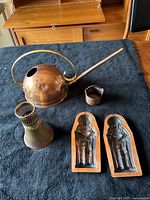 Full view of all 5 copper items set on dark fabric, showing watering can, patinage vase, basket, and chocolate molds