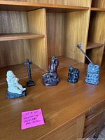 Five stone carvings on a shelf: seated drummer, totem pole, fishing figure, mother and baby, couple.