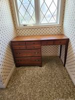 Wooden 4-drawer desk under window in corner.