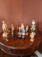 Group photo showing all 11 hand carved wooden figurines, depicting fishermen, duck hunters, and others, arranged on a round wooden table.