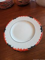 Stack of hand painted plates with white base, black and orange brushstroke rim design.