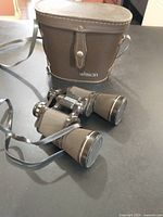 Jason binoculars with textured grips and adjustable focus sitting on a surface next to their brown leather carrying case with strap.