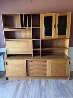 Front view of entire teak wall unit showing upper shelving, drop-down desk, glass-front cabinet, lower drawers and sliding doors.