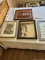 Four framed art pieces on a table covered with white cloth, showing the full variety of the lot