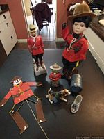 Top-down view of a collection of Mountie themed dolls, figurines, tin can, small shoe, and paper figure with moving parts placed on a table