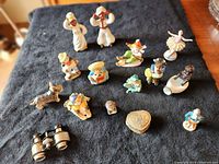 Group photo showing assorted ceramic figurines including African American man and woman, animals, dancers, and inanimate objects along with binoculars and ashtrays on dark fabric background