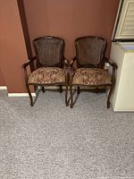 Pair of matching wooden framed armchairs with woven rattan backs and cushioned seats covered in patterned fabric.