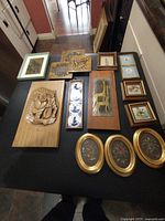 Overall view of 20 assorted wall art pieces including wood reliefs, paintings, tiles, and metal art displayed on table