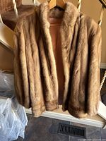 Front view of tawny colored farmed mink jacket hanging on hanger, showing dense fur and collar details.