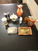 Wide view of all nine Niagara Falls and Expo 67 souvenir items including mugs, pitchers, trays, and decorative containers on a table.