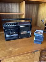 Vintage Magnavox 6-band radio and cassette tape player with six cassette tapes stacked next to it on a wooden shelf.