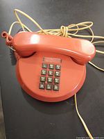 Front view of rust-coloured push-button telephone with handset on top and 12-button keypad.
