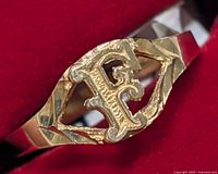 Close-up of the ring showing the ornate letter 'F' in the front with textured design in yellow gold.
