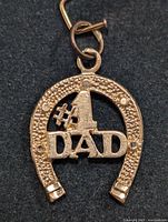 Close-up of gold horseshoe pendant with inscriptions and small ring for chain attachment.