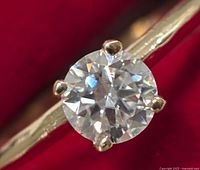 Close-up photo of the solitaire round-cut moissanite gemstone set in a yellow gold ring band, highlighting the gemstone's facets and prongs.