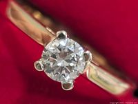 Close-up of round brilliant lab-grown diamond in white gold four-prong setting on yellow gold shank against red background