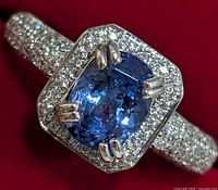 Close-up front view of the silver ring showing oval blue tanzanite center stone with surrounding cubic zirconia halo and shank details.