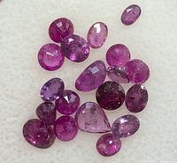 Close-up of faceted ruby gemstones scattered on white cushion showing color variation and inclusions
