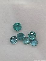 Photo showing six round cut loose emerald gemstones laid flat on white surface.