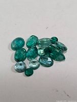 Genuine emerald gemstones in various shapes and sizes shown on a white background.