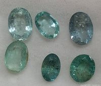 Loose genuine emerald gemstones with natural inclusions, various green shades from light to medium, oval faceted shapes shown in single-layer flat lay.