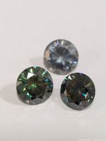 Three round-cut moissanite stones placed on a white background showing their cut, clarity, and light reflection.