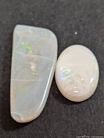 Two polished genuine opal gemstones on black surface, showing their shape and color play