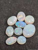 Photo showing eight oval polished genuine opal gemstones on a black background illustrating their colors and translucency.