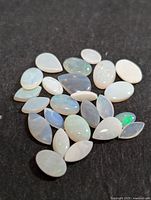 Photo depicting a collection of 22 polished genuine opal cabochon stones on a dark surface showing their varied shapes and play of color.