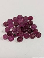 Close-up photo of multiple small faceted ruby beads in pink to deep red hues on a white background.