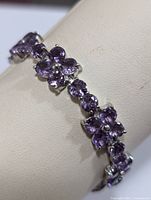 Close-up photo of silver bracelet with purple amethyst stones forming flower shapes, highlighting design and color.