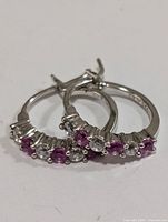 Front angled view of pair of silver hoop earrings with alternating created pink sapphires and clear stones.