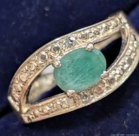 Close-up image of silver ring with oval emerald and small CZ stones on band.