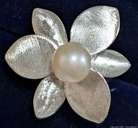 Close-up of silver flower-shaped ring showing six textured petals and a central white pearl on black background