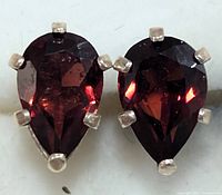 Close-up of both teardrop garnet earrings set in silver with six prongs.