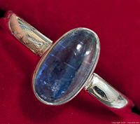 Close-up front view of silver ring with oval blue gemstone on red background showing the polished band and gemstone reflective surface.