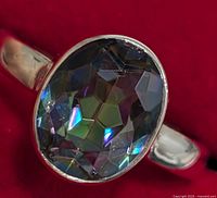 Close-up of the silver ring showing the oval faceted stone with reflective multicolor hues and the polished band.