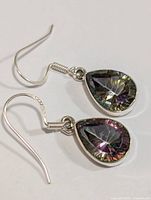 Pair of silver dangle earrings with pear-shaped mystic topaz stones, showing the multicolor iridescent effect and silver hooks.