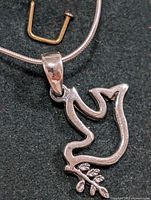 Close-up front view of the hollow silver dove pendant holding a detailed olive branch on a snake chain.