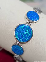 Close-up of silver bracelet with three linked oval opalite stones, showing vibrant blue color with green flecks.