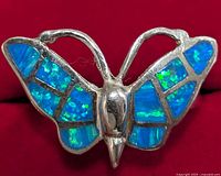 Close-up front view of a silver butterfly ring with blue-green opalite inlay on the wings, showing detailed color and texture of inlay and metal.