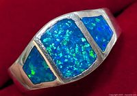 Close-up of silver ring showing large central rectangular and two smaller triangular opalite stones with blue-green iridescence on red background.