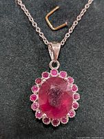 Close-up of oval ruby pendant surrounded by smaller round rubies on silver chain against black background.