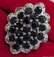 Close-up front view of the silver sapphire cluster ring on red velvet background showing the dark blue gemstones set in a scalloped floral silver base.