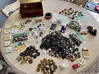 Overview of the button collection spread out on the table including the vintage tin, wooden box, spools of thread, and loose buttons sorted in piles and bags.