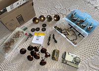 Top-down view of assorted antique drawer pulls, brass knobs, small metal casters, metal decorative circular hardware pieces, vintage door hardware parts with chipped paint.