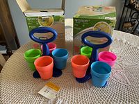 Two Westcott craft utensil holders with four colorful plastic cups each, arranged on a table with original boxes in the background.